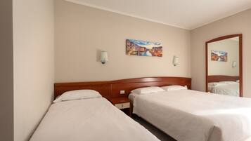 A hotel room with two single beds, a wooden headboard, a nightstand with a lamp, and two wall-mounted lamps.