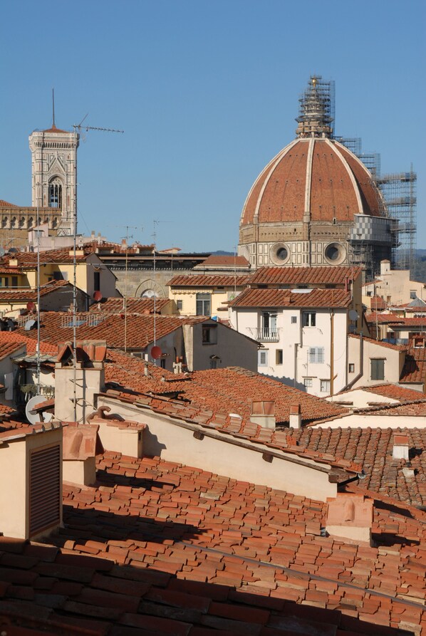 Un edificio histórico con una cúpula y torres de campanas, rodeado de tejados tradicionales con tejas rojas.