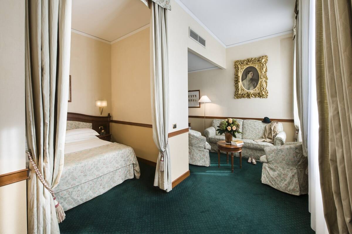 A hotel room with a bed, a sofa, a chair, a small table, and a picture frame on the wall.