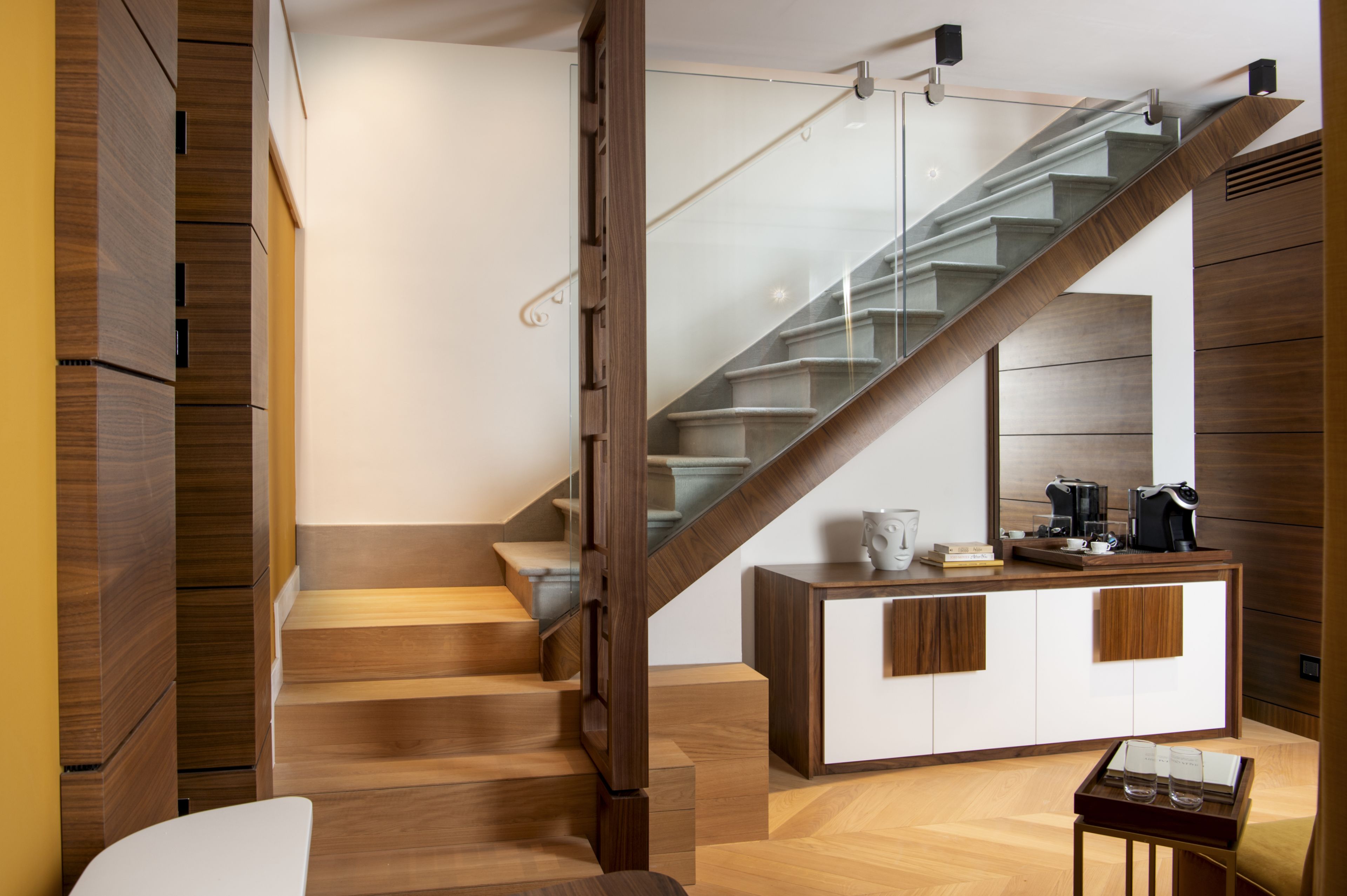 Un escalier moderne avec des rampes en verre, une finition en bois et un espace café intégré comprenant une machine à café et des tasses.