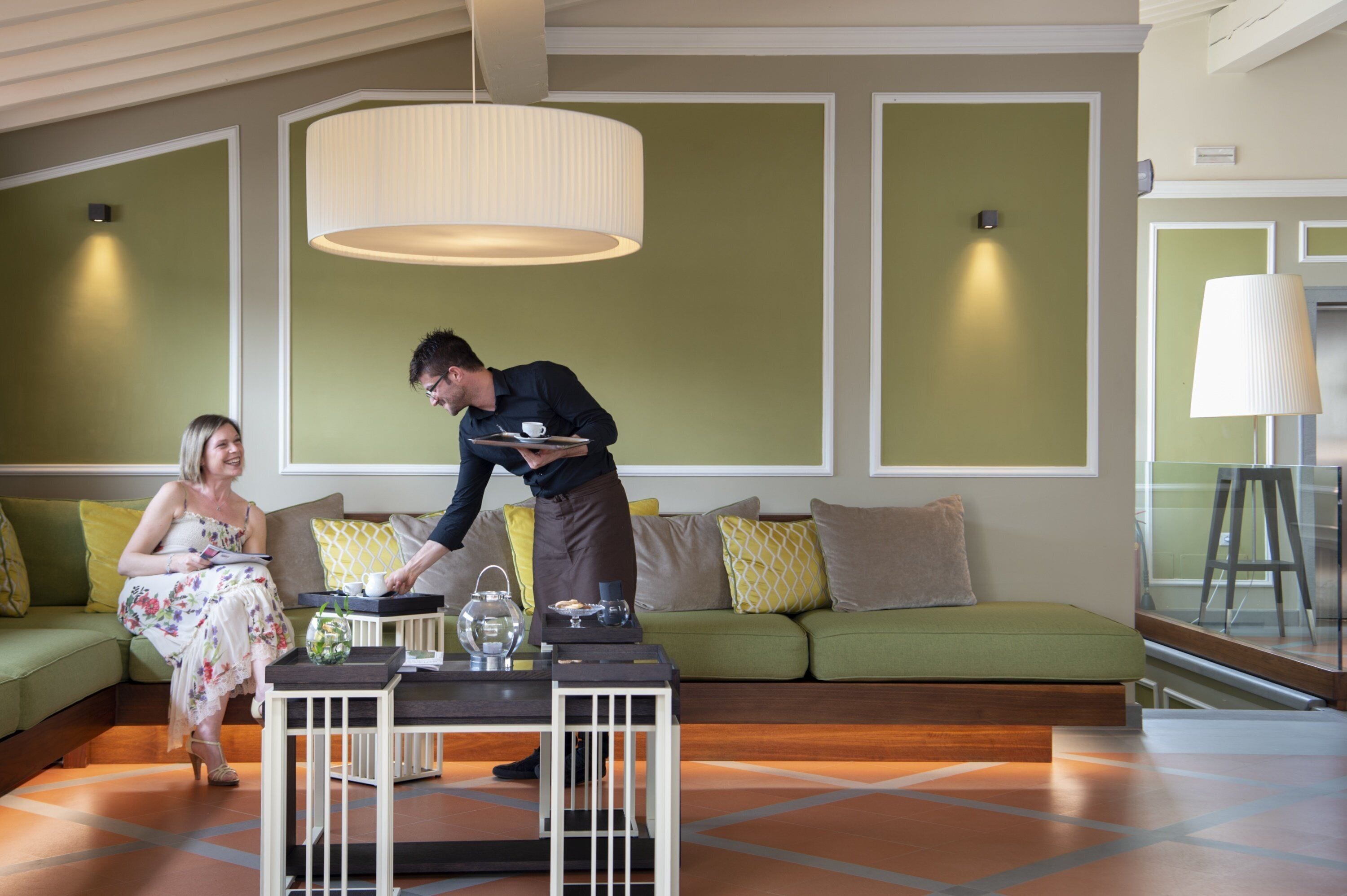Una habitación de hotel moderna con un sofá verde, una mesa de comedor con una tetera y una lámpara colgante grande.