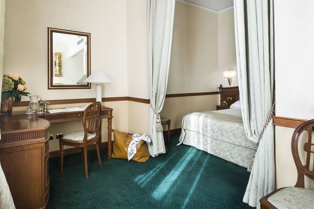 A hotel room with a desk, chair, bed, and a large mirror.