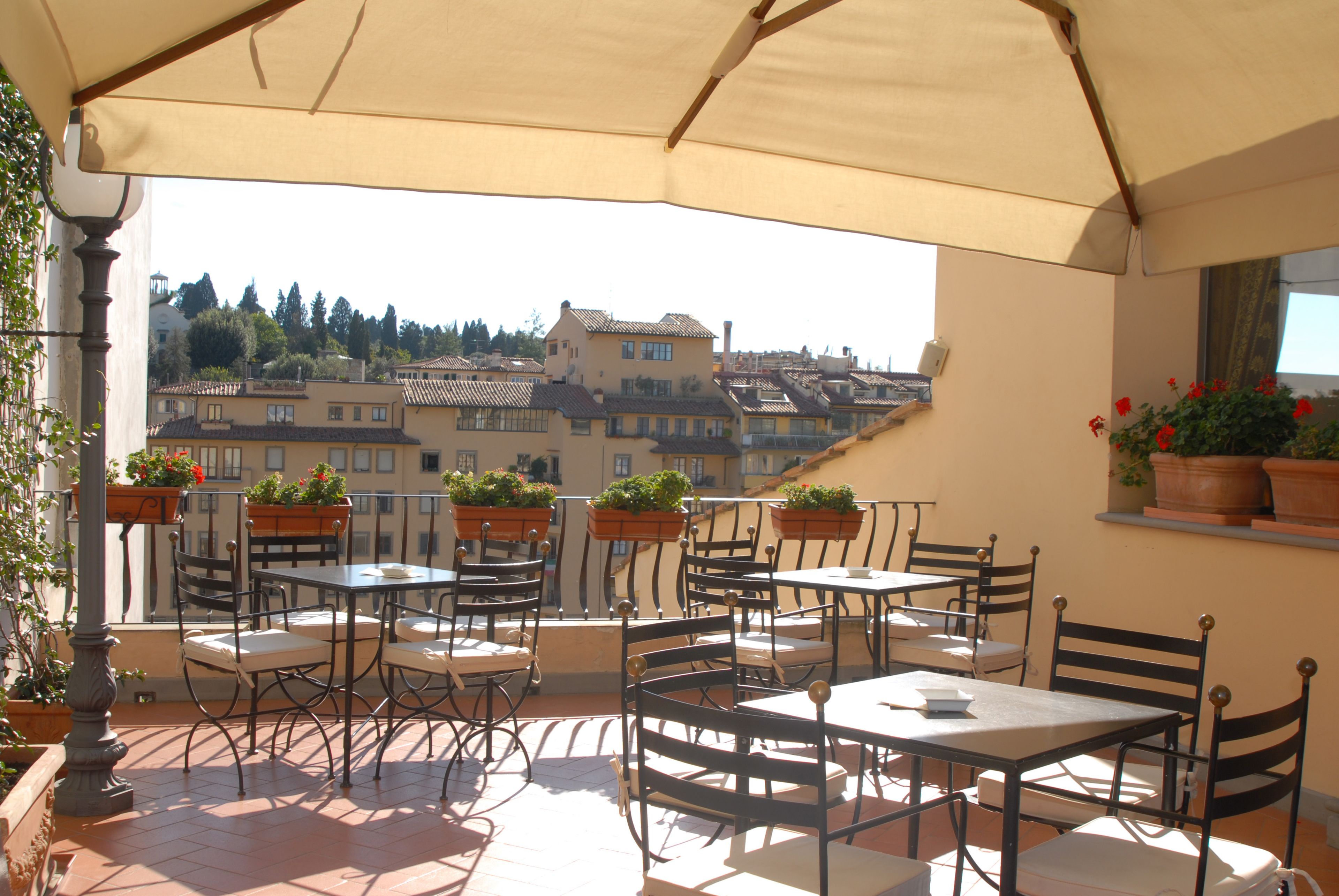 An outdoor terrace with tables and chairs, potted plants, and a view of buildings in the background.