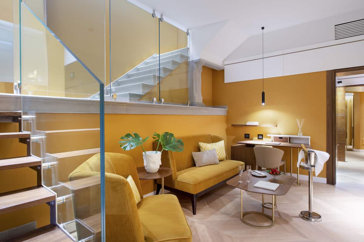 A modern interior with a staircase, a sofa set, a dining table, and a chandelier.