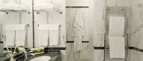 Un baño moderno con paredes de mármol, un lavamanos y una bañera. Hay varias toallas blancas y una bata colgadas en la pared.
