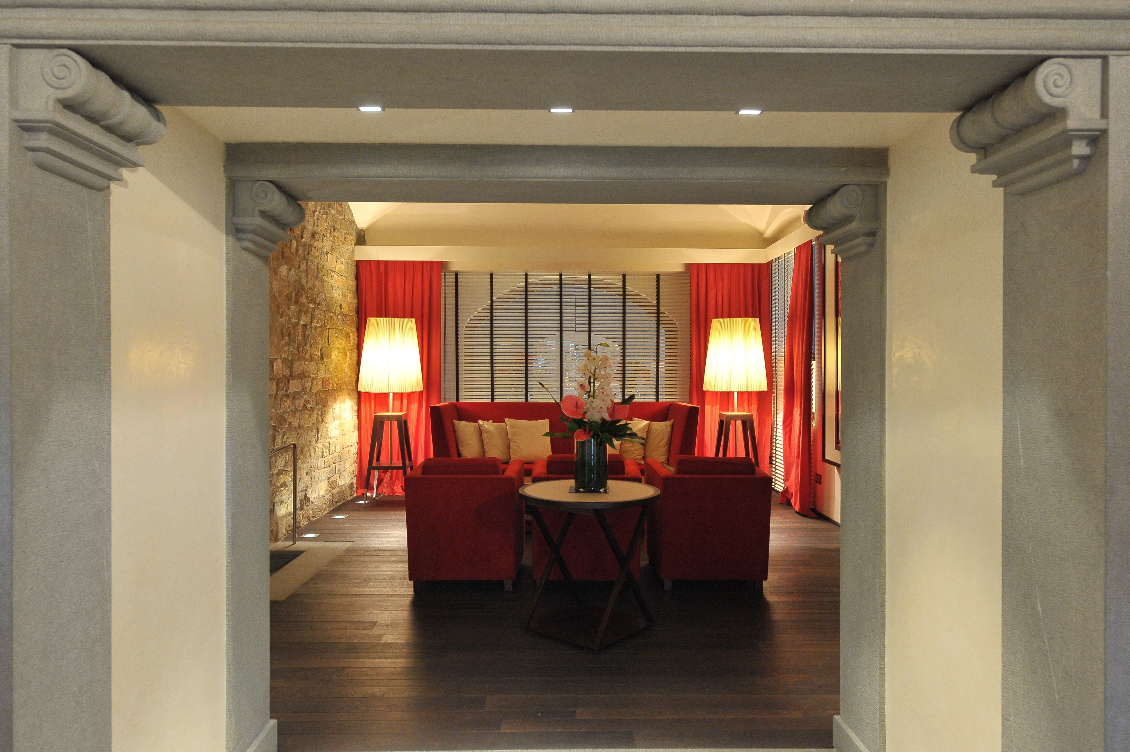 Un hall de hotel con un sofá rojo, una mesa redonda y dos lámparas de pie.