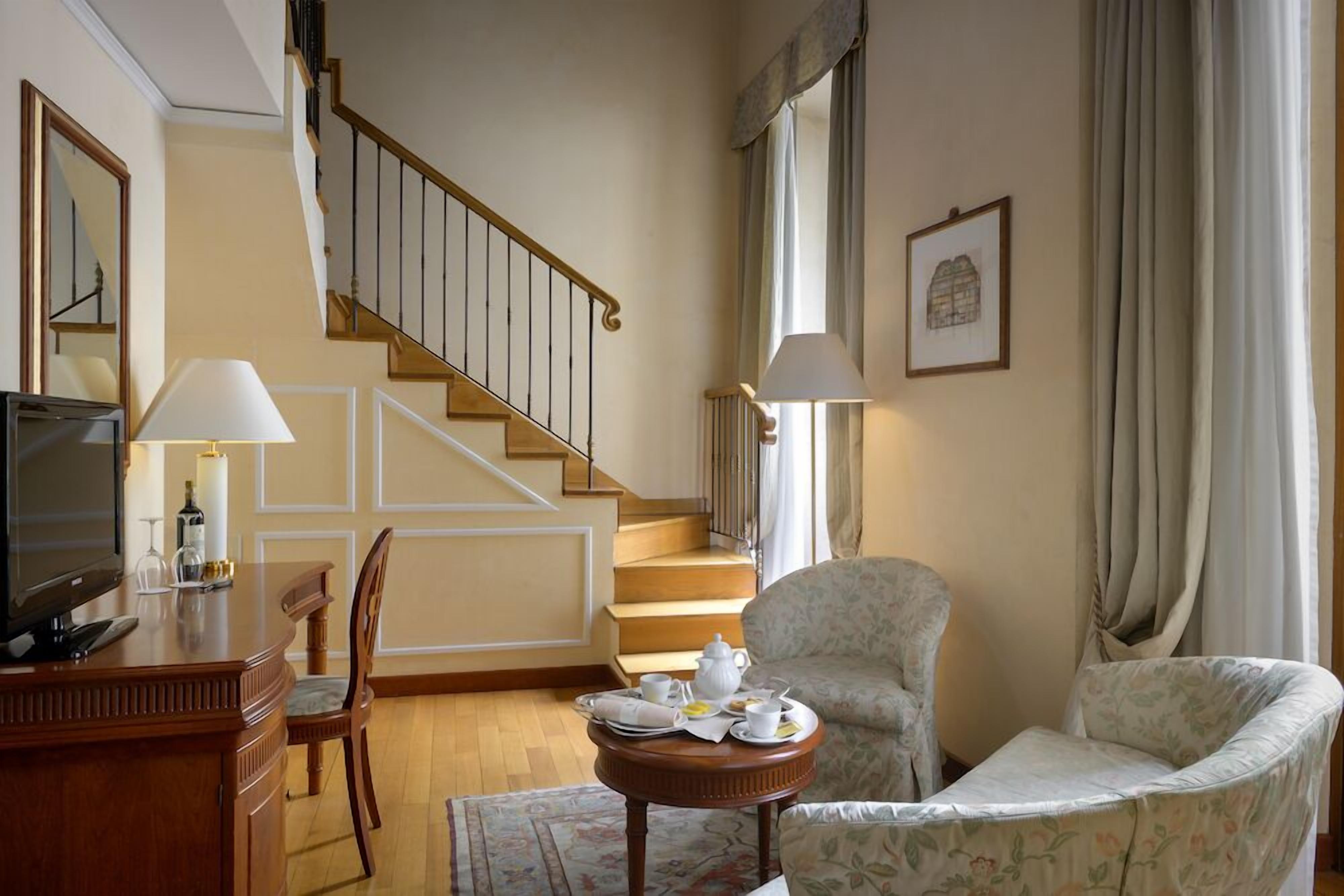 A living room with a wooden staircase, a television, a dining table with a chair, and a sofa.