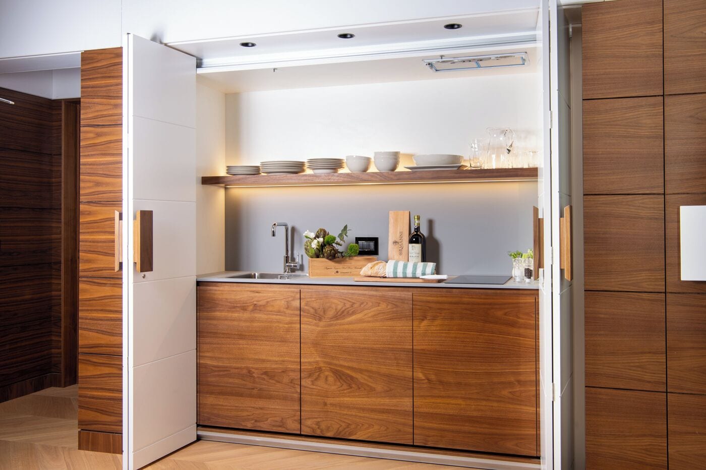 A modern kitchen with wooden cabinetry, a built-in sink, and a countertop with glassware and a bottle.