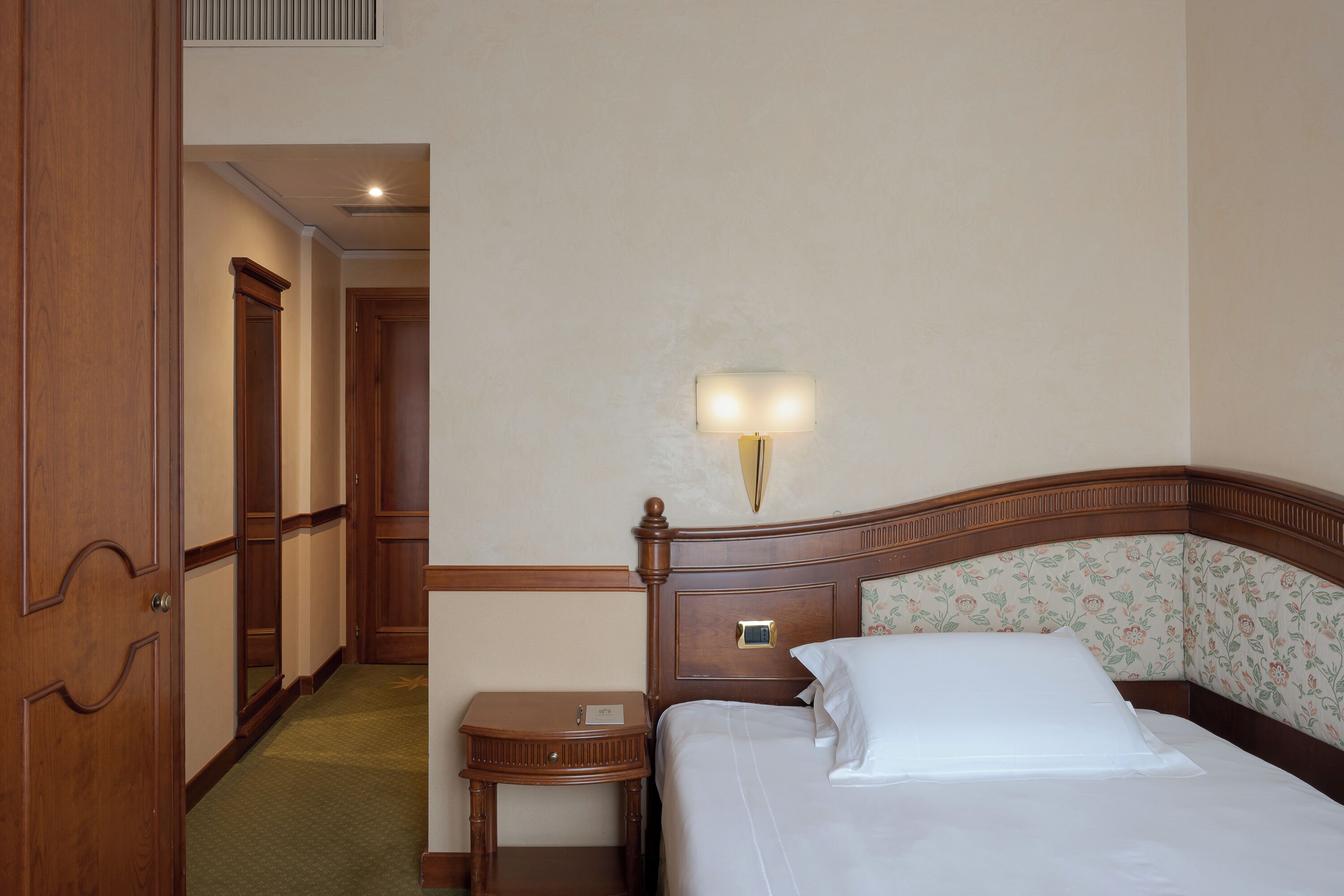 Una habitación de hotel con cabecera de madera, una mesita de noche y un aplique de pared.