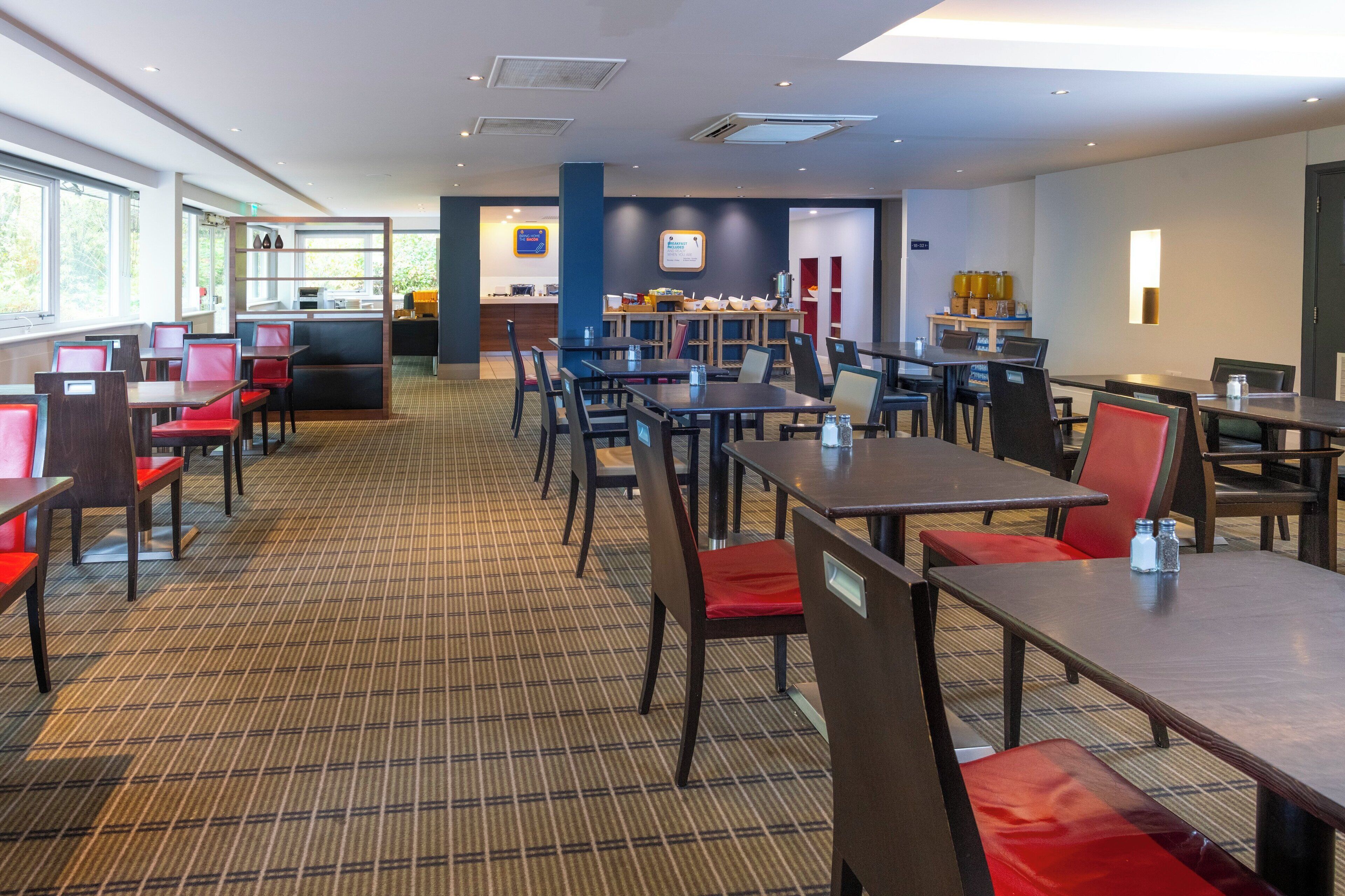 Amplio comedor de hotel con varias mesas y sillas, un mostrador de recepción y una zona de bar.