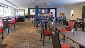 Amplio comedor de hotel con varias mesas y sillas, un mostrador de recepción y una zona de bar.