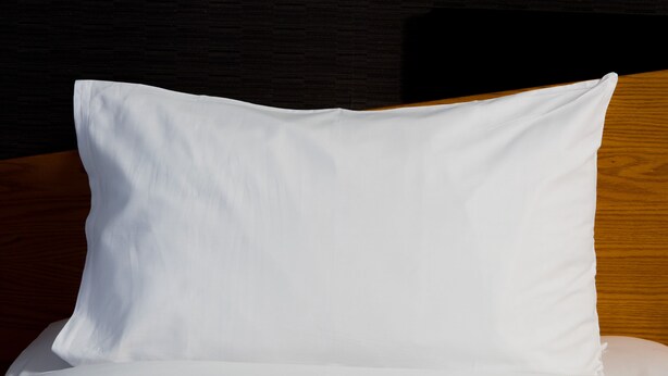 A white pillow on a bed with a wooden headboard.
