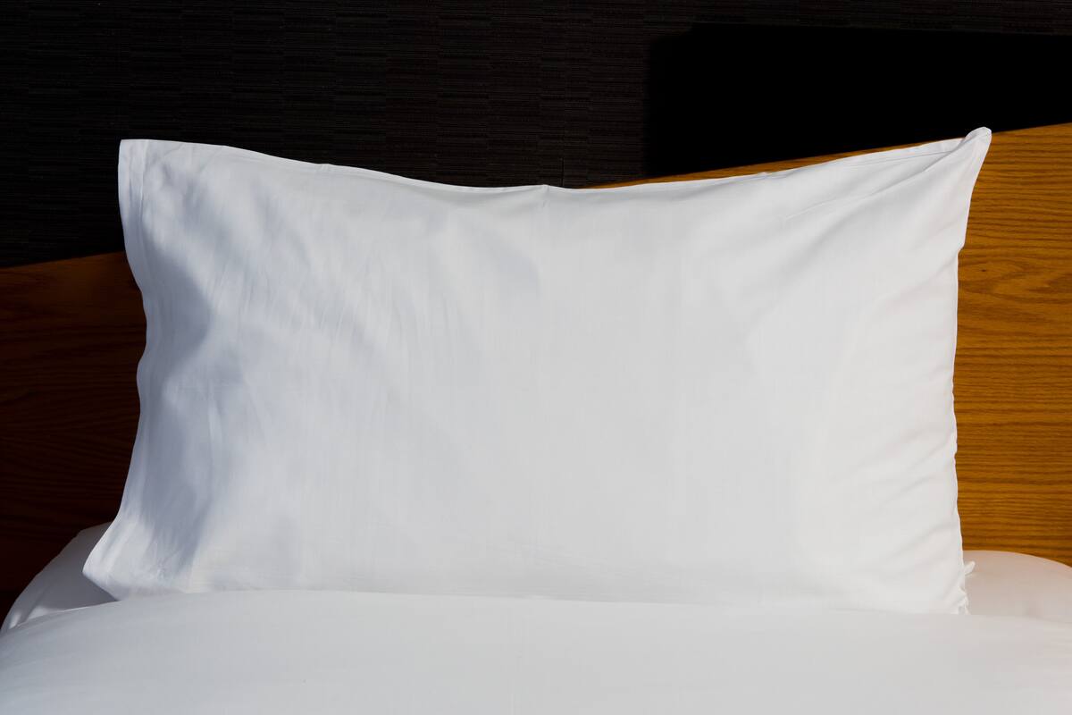 A white pillow on a bed with a wooden headboard.