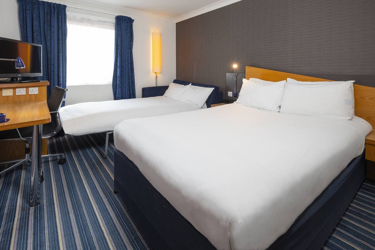 A hotel room with two beds, a desk with a television, and a lamp.