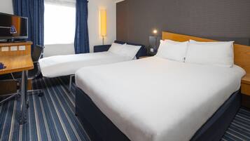 A hotel room with two beds, a desk with a television, and a lamp.