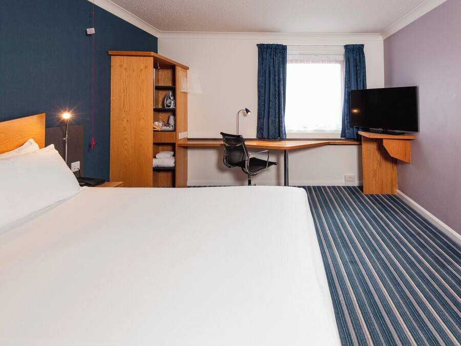 Et hotelværelse med seng, skrivebord, stol, fjernsyn og et klædeskab.
