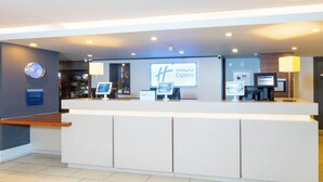 A Holiday Inn Express reception area with a modern design, featuring a reception desk, digital monitors, and a clock on the wall.