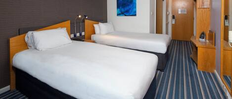 Habitación de hotel con dos camas, un cuadro en la pared y una puerta que da a otra habitación.