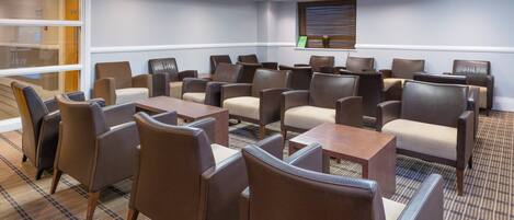 A conference room with multiple tables and chairs, a large window with blinds, and a projector screen on the wall.