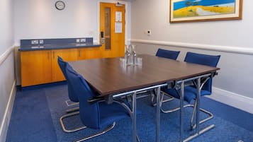 A conference room with a wooden table, blue chairs, a reception desk, and a painting on the wall.