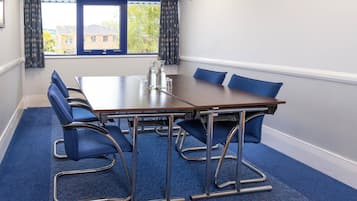 A conference room with a long table, six blue chairs, a pitcher, and glasses on the table.