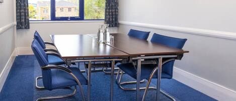 A conference room with a long table, six blue chairs, a pitcher, and glasses on the table.