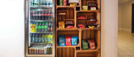 Distributore automatico pieno di bevande e snack, tra cui bibite gassate, acqua in bottiglia e merendine confezionate.