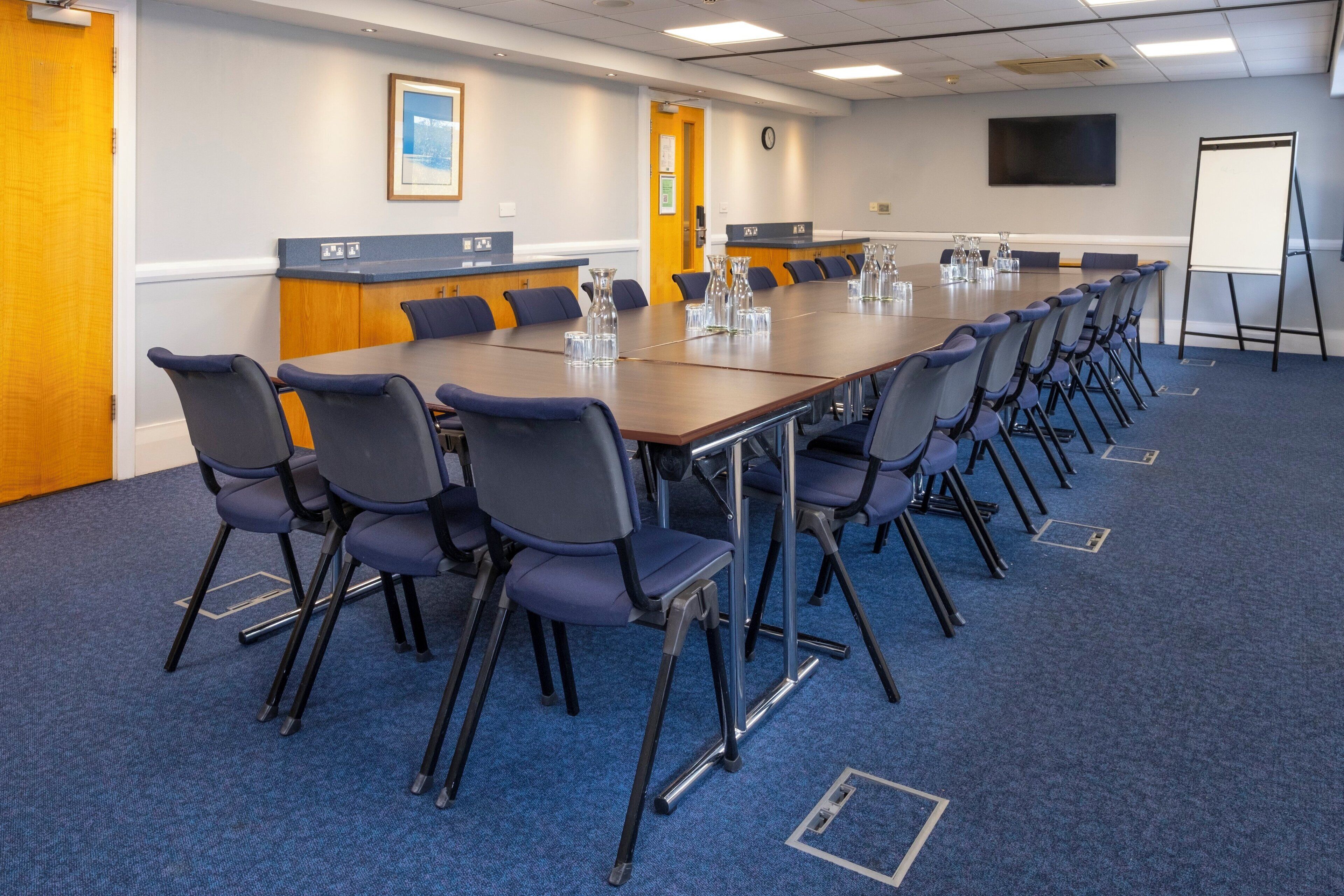 A conference room with a long table, chairs, a whiteboard, and a television on the wall.