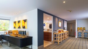 A modern hotel lobby with a reception desk, a buffet area, and a coffee station.