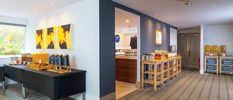 A modern hotel lobby with a reception desk, a buffet area, and a coffee station.