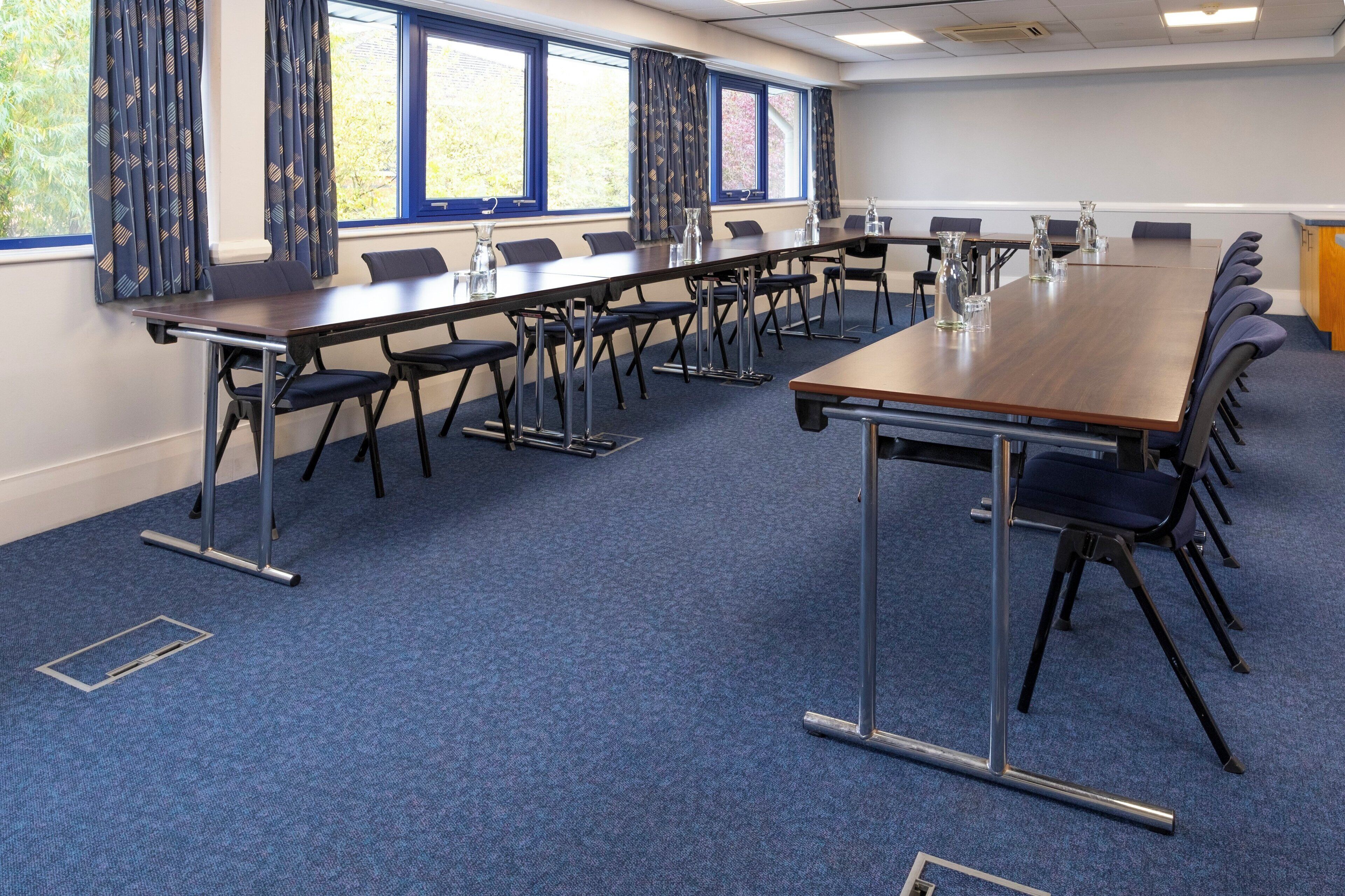 A conference room with a long table, chairs, and a view of trees through the windows.