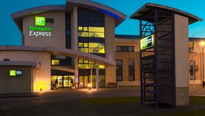 A Holiday Inn Express building with a modern design, a covered entrance, and a visible outdoor seating area.