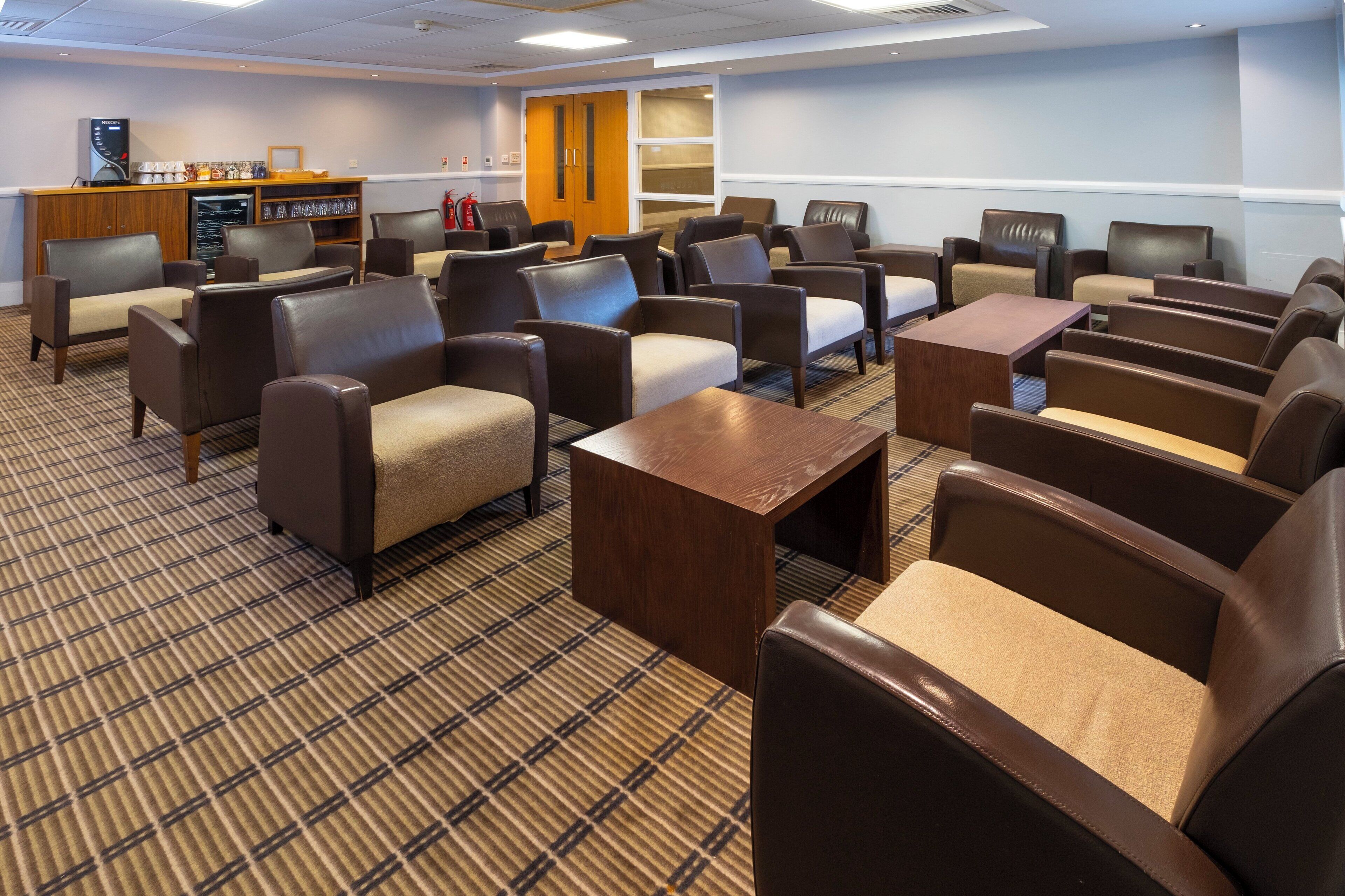 A hotel room with a check-in counter, seating area with sofas and chairs, a small table, and a patterned carpet.