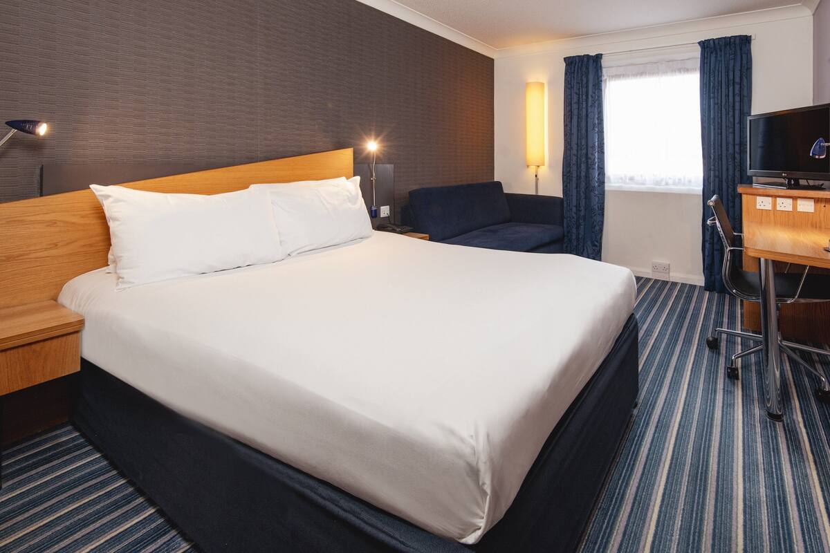 A hotel room with a large bed, a desk with a TV, and a chair.