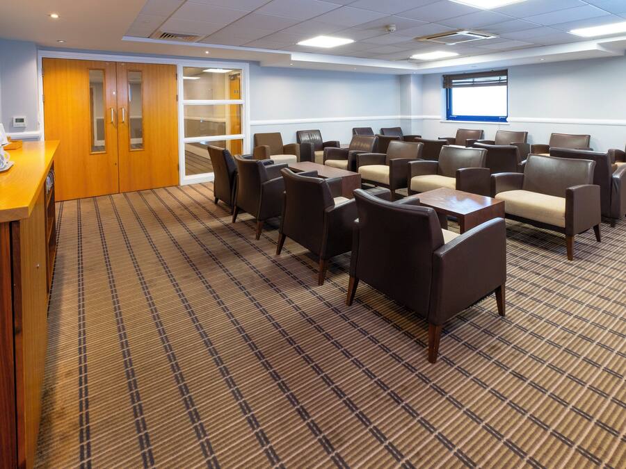 A conference room with a carpeted floor, wooden paneling, and a large screen.