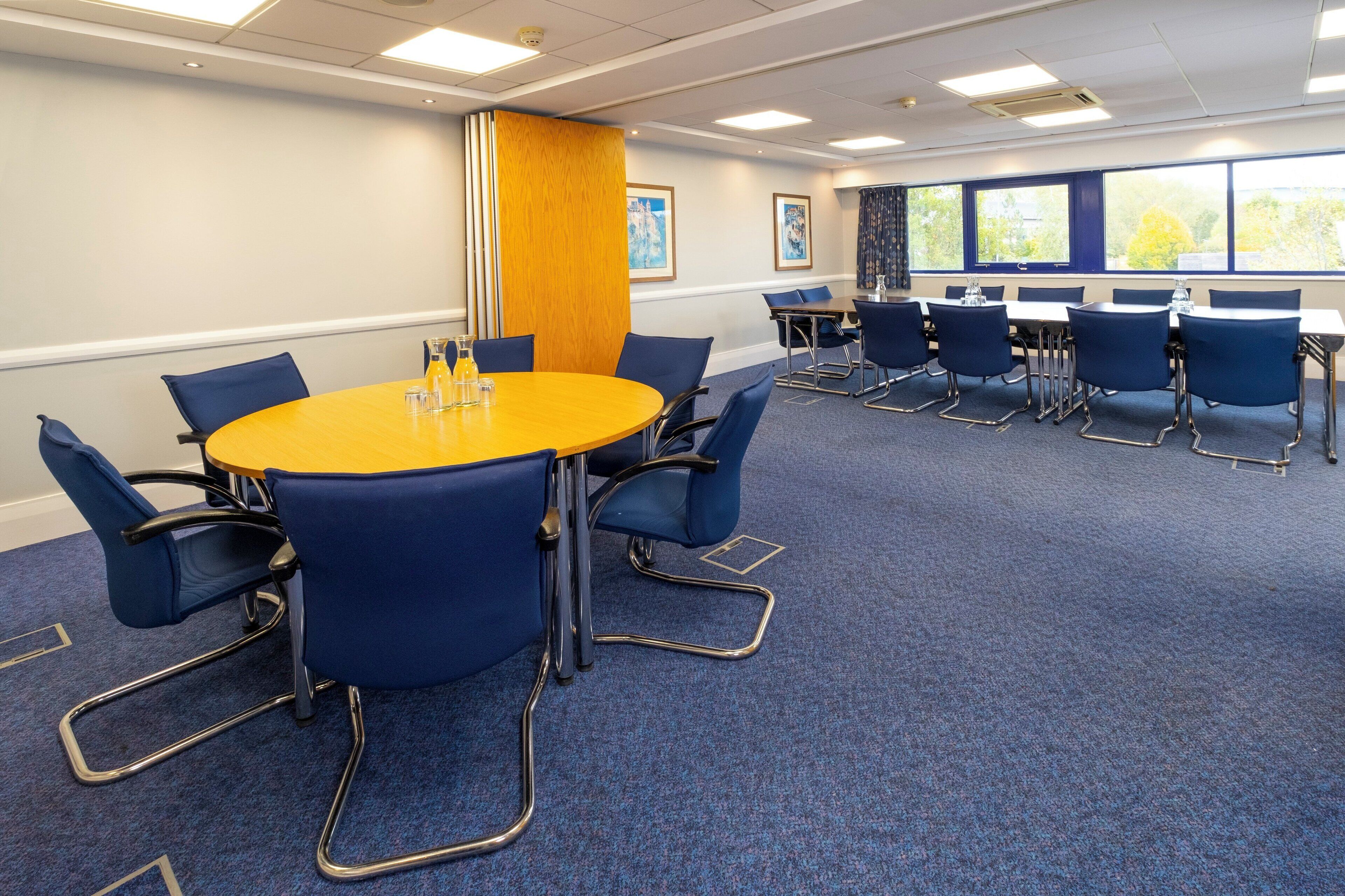 A conference room with a round table, blue chairs, and a carpeted floor.