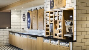 A café with a counter, menu boards, and a coffee machine. - Holiday Inn Express London - Park Royal by IHG (London)