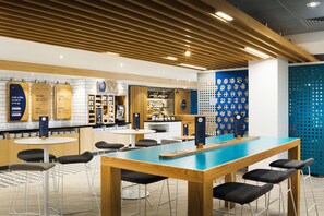 A modern cafe interior with wooden tables, black cushioned chairs, and a blue accent wall. - Holiday Inn Express London - Park Royal by IHG (London)
