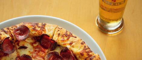 A pizza with pepperoni slices on a white plate, accompanied by a glass of beer on a wooden table.