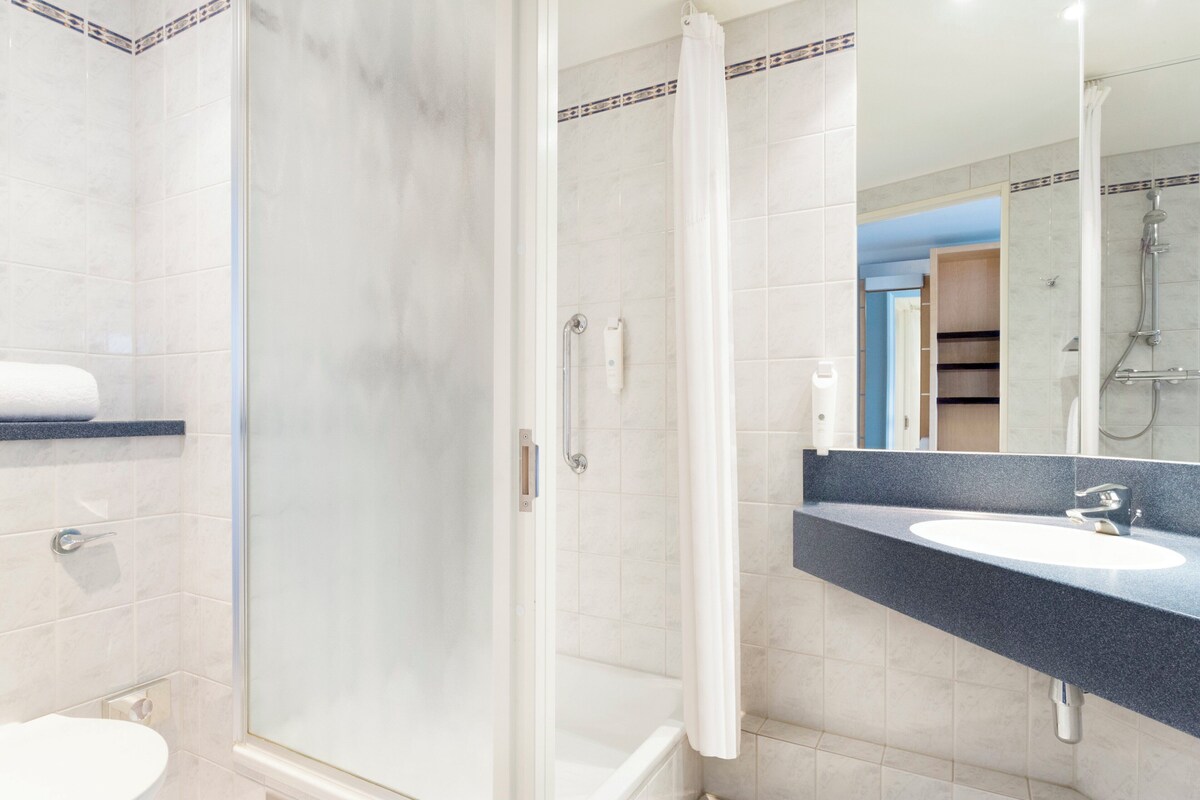 Une salle de bain avec une douche à parois de verre, un lavabo blanc et un miroir au-dessus du lavabo.