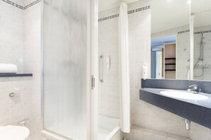 Une salle de bain avec une douche à parois de verre, un lavabo blanc et un miroir au-dessus.
