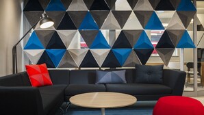 A modern office space with a sectional sofa, a round wooden table, and a geometric patterned wall. - Holiday Inn Express London - Park Royal by IHG (London)