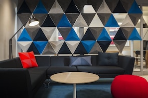 A modern office space with a sectional sofa, a round wooden table, and a geometric patterned wall. - Holiday Inn Express London - Park Royal by IHG (London)