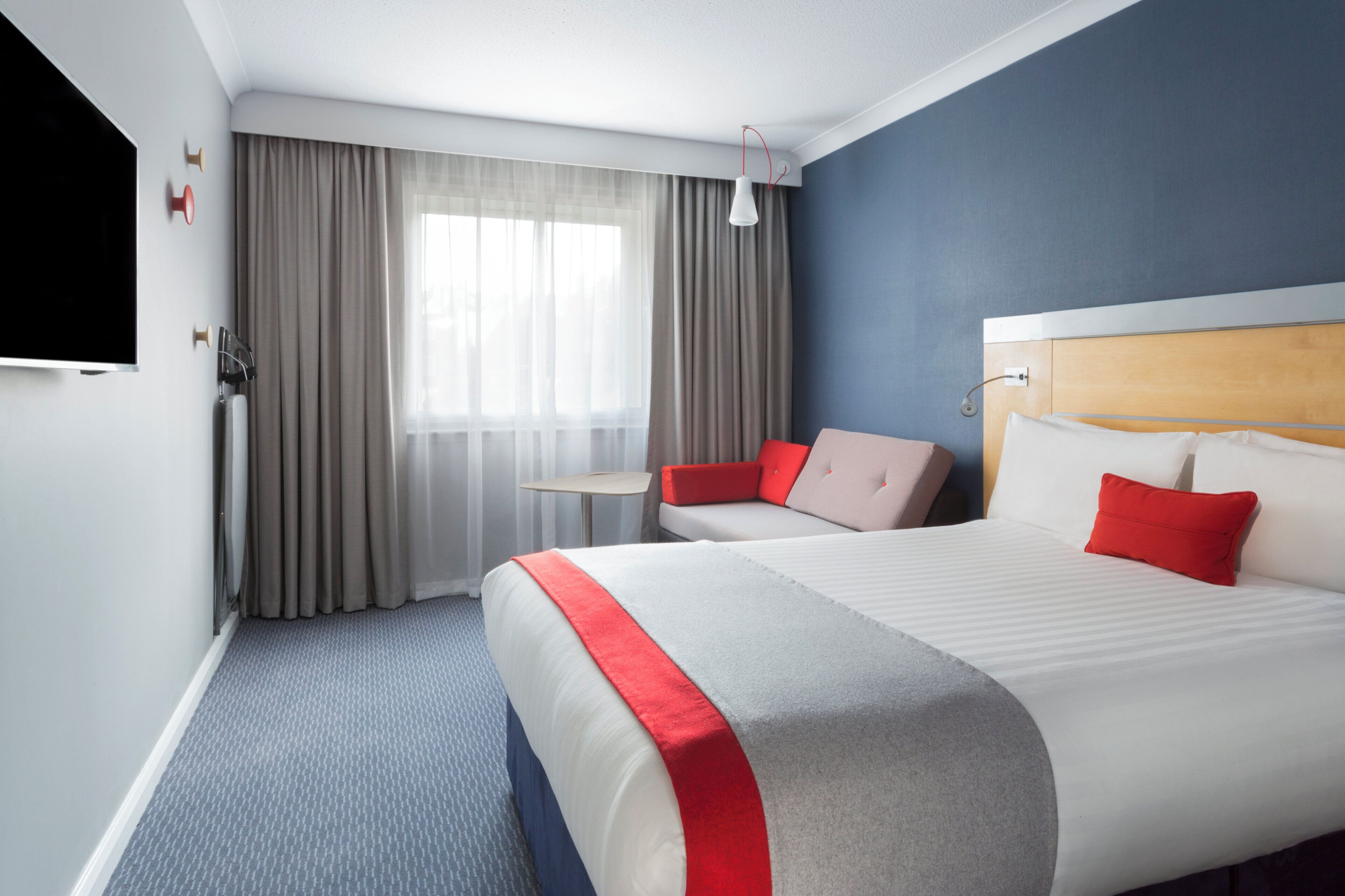 Una camera d'albergo con un letto grande, una televisione, un tavolino e una finestra con tende.