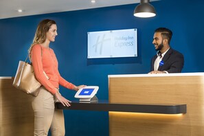 A reception desk with a digital screen displaying 'Holiday Inn Express' branding, a person interacting with the screen, and a wooden reception counter. - Holiday Inn Express London - Park Royal by IHG (London)