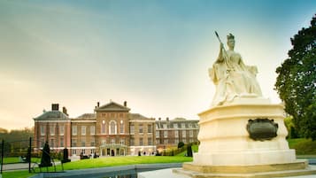 A classical statue in a garden with a large brick building in the background.