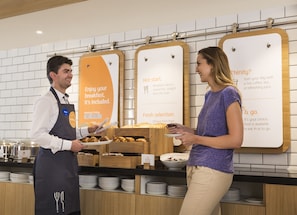 A breakfast counter with a menu board, a server, and a customer. - Holiday Inn Express London - Park Royal by IHG (London)