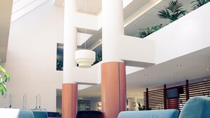 A spacious lobby with high ceilings, large pillars, and a mezzanine level with plants.