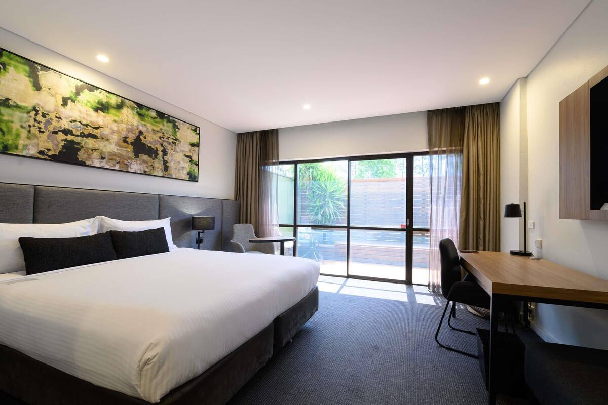 A hotel room with a large bed, a desk, a chair, a TV, and a view through the window.