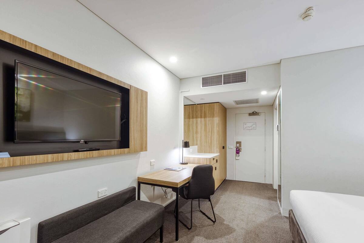 A modern hotel room with a flat-screen TV, a desk with a chair, a sofa, and a bed.
